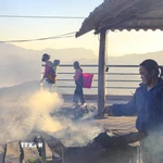 Khói bếp hòa trong sương sớm khi một phụ nữ chuẩn bị đồ nướng phục vụ khách chợ phiên. (Ảnh: Xuân Tư/TTXVN)