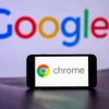 Biểu tượng Chrome trên màn hình điện thoại và biểu tượng Google (phía sau). (Ảnh: Getty Images/TTXVN)