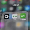 Ứng dụng Grab (giữa) và Uber (trái) trên điện thoại di động. (Nguồn: THX/TTXVN)