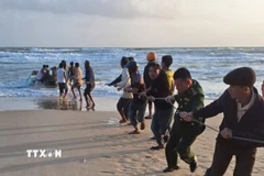 Các lực lượng chức năng và người dân triển khai kéo ghe vào bờ. (Ảnh: TTXVN phát)