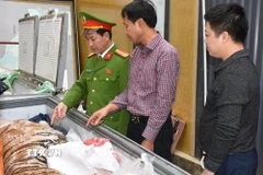 Đối tượng Hoàng Đình Đạt mặc áo kẻ sọc màu đỏ cùng tang vật vụ án. (Ảnh TTXVN phát)