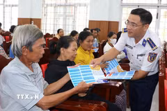 Cảnh sát biển phát tờ rơi tuyên truyền chống khai thác bất hợp pháp cho bà con ngư dân. (Ảnh: Đinh Hương/TTXVN)