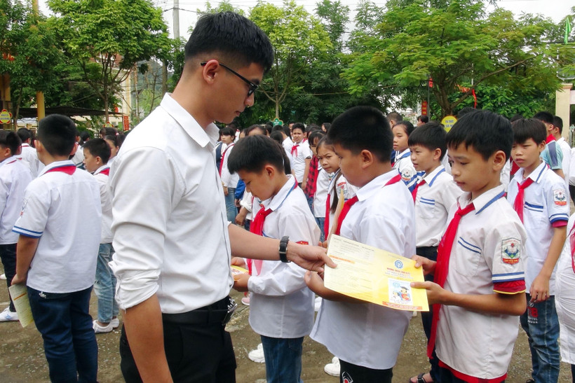 Cán bộ bảo hiểm phát tờ rơi tuyên truyền về bảo hiểm y tế học sinh. (Ảnh: Hữu Quyết/TTXVN)