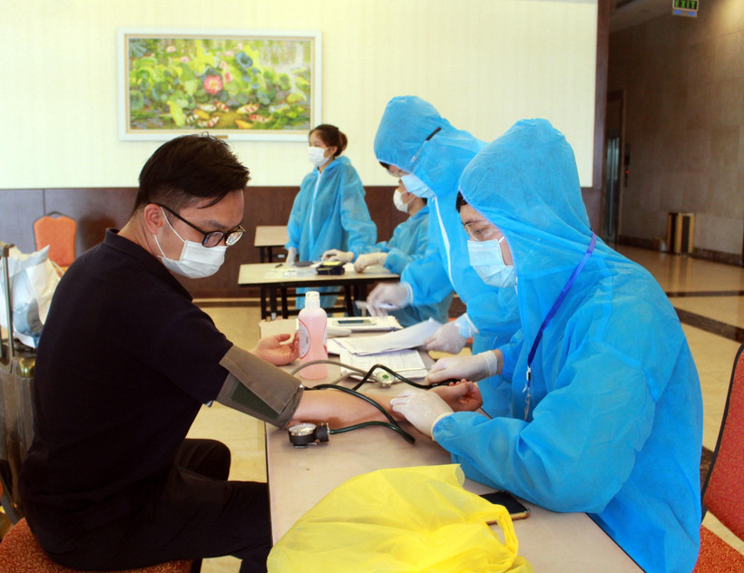 Nhân viên y tế hướng dẫn chuyên gia, lao động nước ngoài khai báo y tế và kiểm tra sức khỏe trước khi vào khách sạn cách ly. (Ảnh: TTXVN)