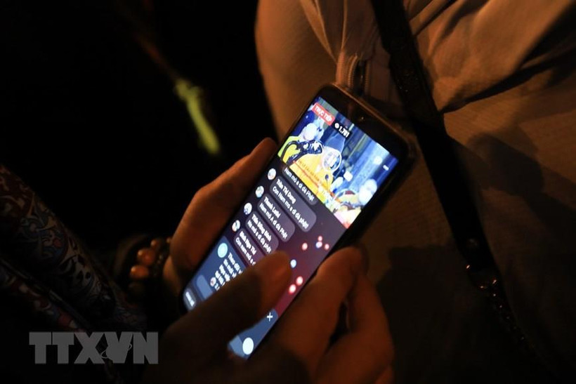 Người dân theo dõi lễ cầu an trực tuyến qua điện thoại di động. (Ảnh: Thành Đạt/TTXVN)