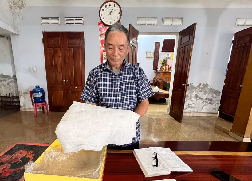 Ông Nguyễn Đình Tính nâng niu tấm màn được "người anh lớn" Tổng Bí thư Nguyễn Phú Trọng tặng nhân dịp về thăm xã Vạn Thọ vào năm 2005. (Ảnh: Hạnh Nguyễn/Vietnam+)