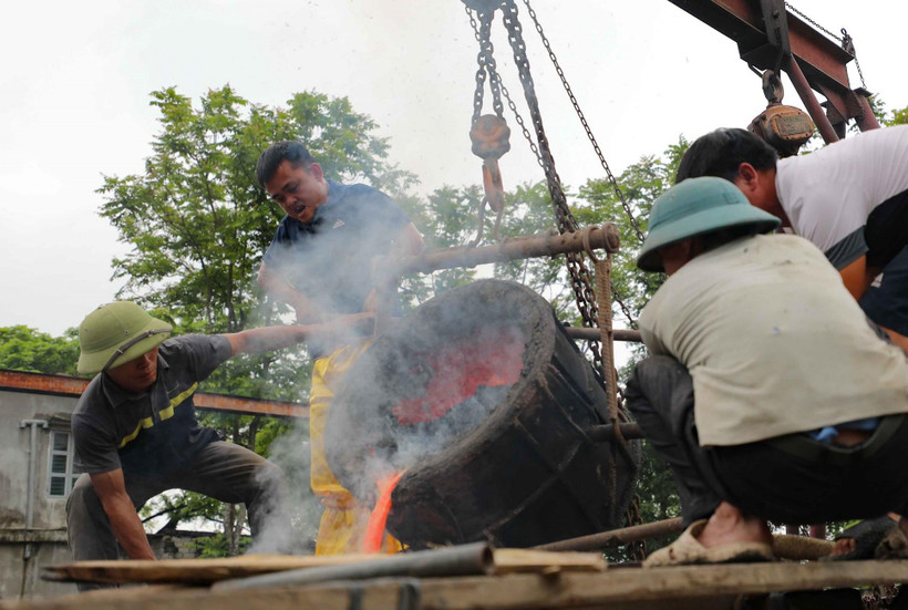 Các nghệ nhân thực hiện rót đồng vào khuôn trống. (Ảnh: Thanh Tùng/TTXVN)