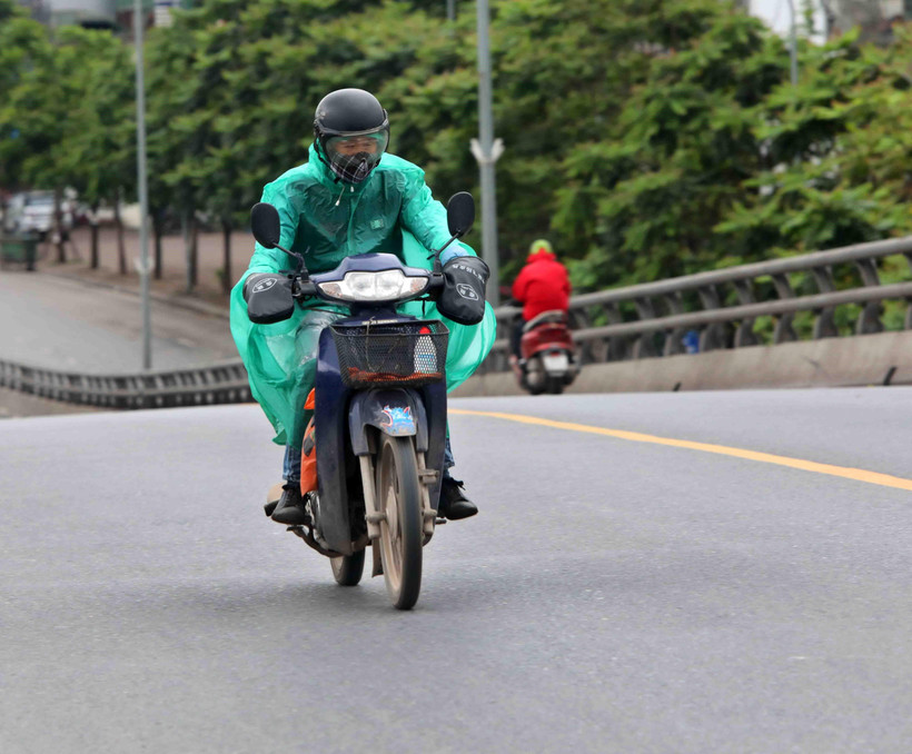 Người đi đường phải mặc thêm áo mưa để bớt gió lạnh. (Ảnh: Thanh Tùng/TTXVN)