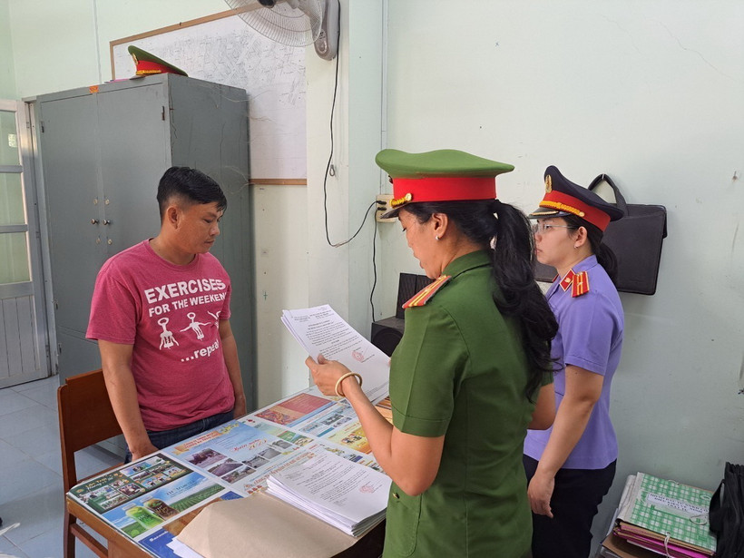 Lực lượng chức năng tống đạt các Quyết định và Lệnh bắt tạm giam đối tượng Phan Thành Được (trái, áo đỏ). (Ảnh: TTXVN phát)