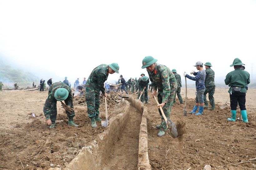 Các chiến sỹ thuộc Trung đoàn 82, nạo vét kênh mương, thu gom đất đá giúp người dân vùng lũ Mường Pồn sớm khôi phục sản xuất. (Ảnh: Phan Quân/TTXVN)