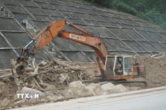 Đơn vị thi công phải dùng xe máy chuyên dụng để phá các tảng đá lớn nặng hàng chục tấn bị nước lũ cuốn lăn xuống đường. (Ảnh: Quốc Dũng/TTXVN)