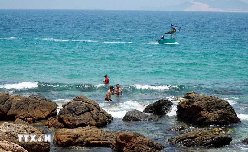 Du khách thích thú hòa mình vào làn nước biển trong xanh cạnh khu vực Mũi Vi Rồng. (Ảnh: Lê Phước Ngọc/TTXVN)