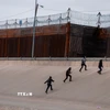 Những người di cư chuẩn bị vượt qua bức tường biên giới Mỹ-Mexico. (Ảnh: THX/TTXVN)