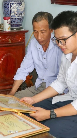 Em Trần Xuân Đam và bố giới thiệu những tấm bằng khen đã đạt được trong quá trình học tập. (Ảnh: Công Luật/TTXVN)
