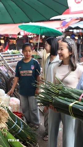 Chị Phạm Thu Hương, 56 tuổi, Việt kiều tại Lào, hướng dẫn các con cách chọn lá dong gói bánh chưng. (Ảnh: Xuân Tú/TTXVN)