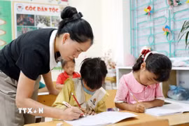 Giáo viên Trường Phổ thông Dân tộc Bán trú Tiểu học và Trung học cơ sở Thu Lũm hướng dẫn học sinh lớp 1 tập viết chữ. (Ảnh: Quý Trung/TTXVN)