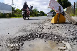 Người dân đặt vật dụng cảnh báo người lái xe né tránh các ổ gà, ổ voi trên quốc lộ 80. (Ảnh: Văn Sĩ/TTXVN)