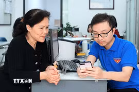 Đoàn viên thanh niên phường Hàng Bồ (quận Hoàn Kiếm, thành phố Hà Nội) hỗ trợ người dân thực hiện thủ tục hành chính công trên thiết bị điện thoại thông minh. (Ảnh: Phạm Hậu/TTXVN)