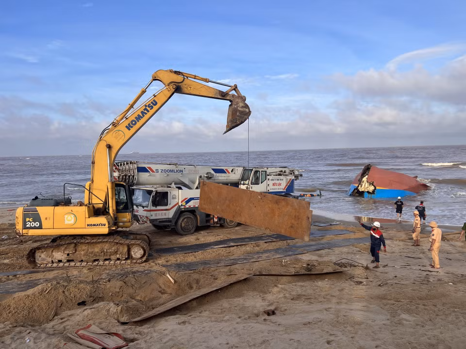 Xe máy múc vận chuyển những tấm thép lớn làm đường cho xe cần cẩu hạng nặng tiếp cận tàu bị nạn. (Ảnh: Nguyên Linh/TTXVN)