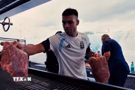 Lautaro Martínez phụ giúp đặt các miếng thịt lên vỉ nướng trong bữa tiệc asado của đội tuyển Argentina. (Ảnh: Infobae)