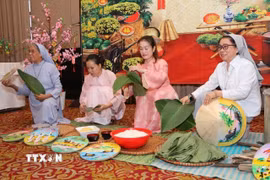 Các sơ cùng đại diện cộng đồng mô phỏng nét đẹp gói bánh chưng tại buổi lễ. (Ảnh: TTXVN phát)
