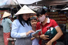 Tổ công nghệ số Đoàn Thanh niên xã Long Sơn cài đặt và hướng dẫn tiểu thương tại khu vực bán hàng hải sản phía trước Nhà lớn Long Sơn. (Ảnh: Đoàn Mạnh Dương/TTXVN)