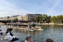 Tàu du lịch trên sông Seine đi qua những khu phố cổ của Paris, trong khi người dân ngồi nghỉ ngay sát mép nước. (Ảnh: Hữu Chiến/TTXVN)