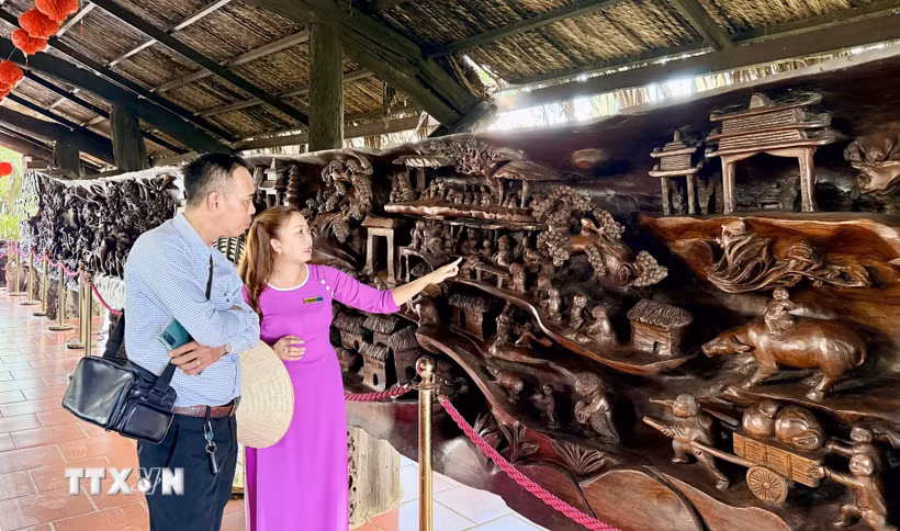 Du khách tham quan bức tranh gỗ lũa khổng lồ dài gần 25m, nặng khoảng 20 tấn, được xem là một trong những tác phẩm công phu bậc nhất Việt Nam. (Ảnh: Thanh Sang/TTXVN)