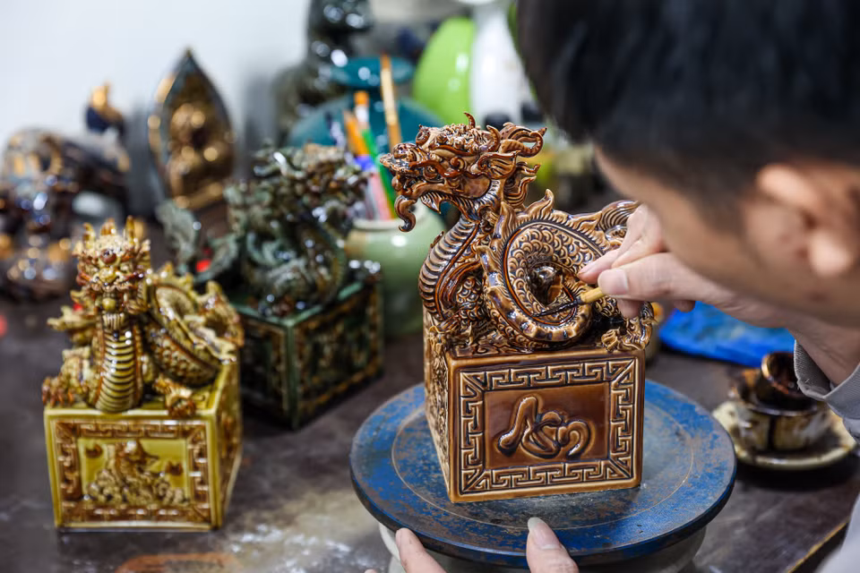 Anh Mạc Triều Dương, một thợ thủ công cho biết mỗi sản phẩm rồng sẽ được vẽ hoàn thiện trong khoảng 2 tiếng rưỡi. Mỗi ngày một thợ thủ công có thể hoàn thiện được 5-6 sản phẩm. Người thợ sẽ dùng dung dịch vẽ vàng 24K để trang trí cho sản phẩm sau đó sẽ được mang đi nung lần 2 ở nhiệt độ phù hợp trong khoảng 6-8 tiếng để tạo nên lớp mạ vàng sang trọng. (Ảnh: Minh Sơn/Vietnam+)