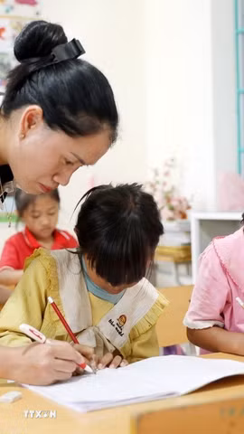 Giáo viên Trường Phổ thông Dân tộc Bán trú Tiểu học và Trung học cơ sở Thu Lũm hướng dẫn học sinh lớp 1 tập viết chữ. (Ảnh: Quý Trung/TTXVN)