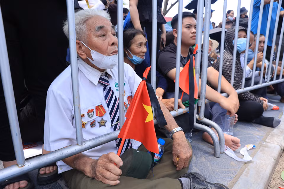 Một cựu chiến binh mang theo cờ rủ chờ đưa tiễn Tổng Bí thư. (Ảnh: Hoài Nam/Vietnam+)