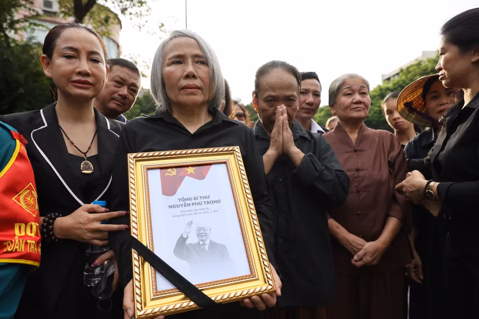 Bà Trần Thị Hậu sinh năm 1969 ở huyện Hoài Đức, Hà Nội, đã đưa các cháu mình đến xếp hàng từ 11h trưa nhưng do trời mưa nên bà đưa cháu về. Bà quay lại lúc 16h chiều để được vào viếng Tổng Bí thư. (Ảnh: Minh Sơn/Vietnam+)