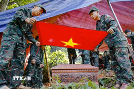 Chiến sỹ phủ cờ Tổ quốc lên tiểu sành đựng hài cốt liệt sỹ. (Ảnh: Xuân Tư/TTXVN)