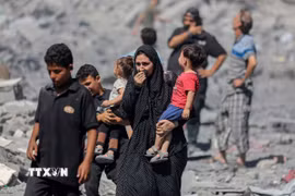 Người dân Palestine đứng trên đống đổ nát sau các cuộc không kích của Israel xuống Dải Gaza. (Ảnh: IRNA/TTXVN)
