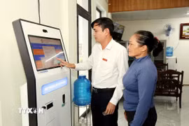Cán bộ Trung tâm phục vụ hành chính công hỗ trợ người dân lấy số thứ tự giải quyết thủ tục hành chính. (Ảnh: Tá Chuyên/TTXVN)