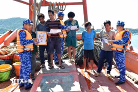 Vùng Cảnh sát biển 4 tặng cờ Tổ quốc, ảnh Bác Hồ cho ngư dân và phát tờ rơi tuyên truyền về khai thác IUU. (Ảnh: TTXVN phát)