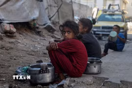 Trẻ em ngồi chờ nhận thức ăn cứu trợ ở thành phố Gaza. (Ảnh: THX/TTXVN)