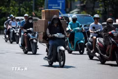 Người giao hàng bằng xe máy phải phủ kín người bằng áo chống nắng, khẩu trang và mũ để thích nghi với thời tiết khắc nghiệt. (Ảnh: Phạm Tuấn Anh/TTXVN)