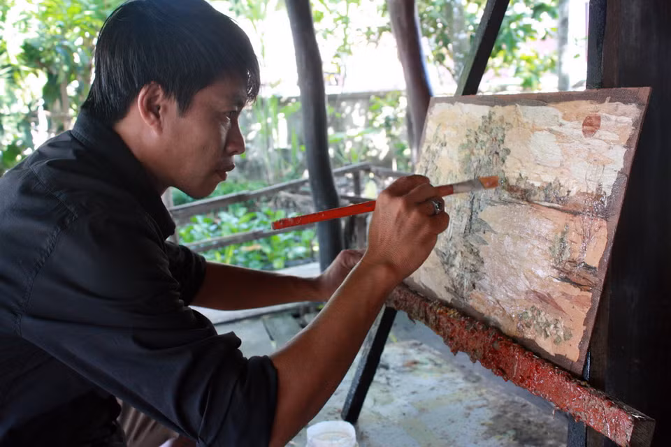 Anh Lê Hoàng Nhân phác họa bức tranh làm từ vỏ tràm. (Ảnh: Lê Sen/TTXVN)