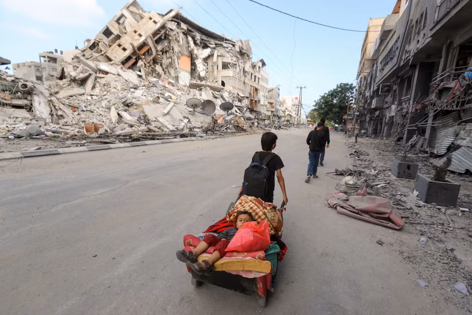 Một cậu bé người Palestine kéo xe chở em trai và đồ đạc, chạy trốn khỏi nhà trong các cuộc tấn công bằng không quân và pháo binh của Israel. (Ảnh: Reuters)