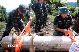 Cán bộ, chiến sỹ chuyên ngành cẩn trọng thực hiện kiểm tra bom CBU-87 trước khi đưa xuống hố hủy nổ. (Ảnh: Thanh Hải/TTXVN)