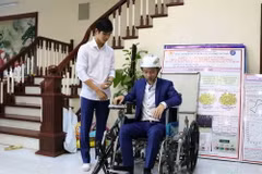 Em Nguyễn Hữu Thành Đạt (bên trái) và Nguyễn Công Khánh thử nghiệm xe lăn leo cầu thang điều khiển bằng cử chỉ của đầu, giọng nói và điện thoại thông minh. (Ảnh: Thanh Thương/ TTXVN)