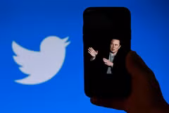 Chân dung tỷ phú Elon Musk trên màn hình điện thoại và biểu tượng Twitter (phía sau). (Ảnh: AFP/TTXVN)