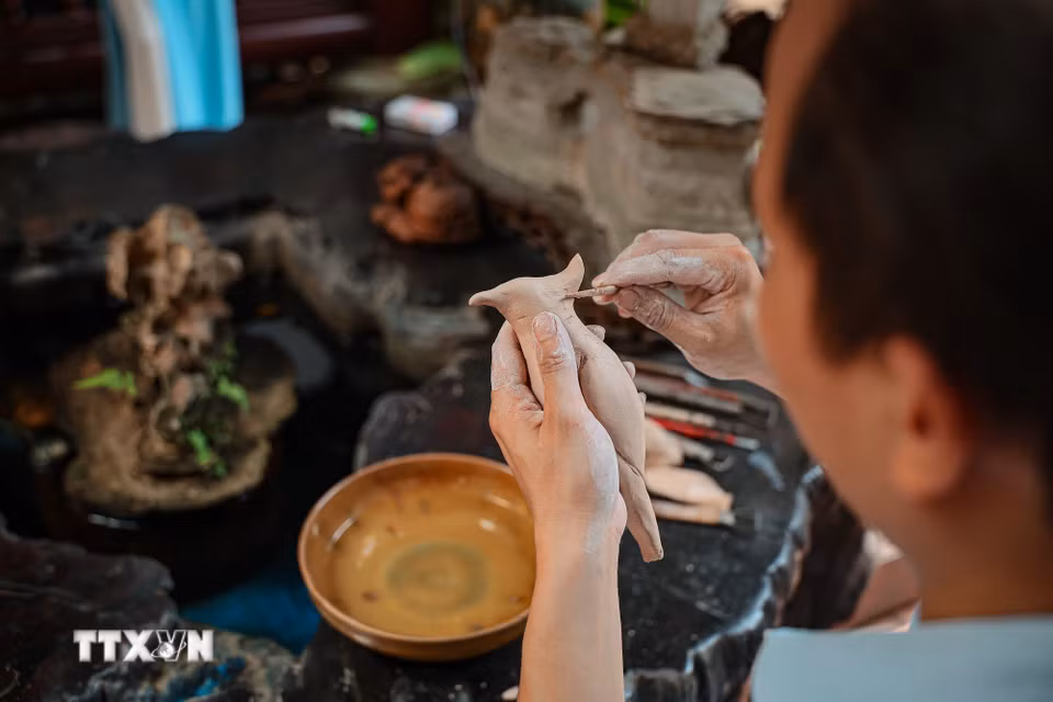 Đôi tay nghệ nhân Bùi Văn Tự tỉ mỉ tạo các chi tiết trên mẫu chim bằng đất sét. Hình ảnh chim, cá, cây trái và hoa sen được anh đưa vào tác phẩm để kể những câu chuyện về gia đình, quê hương. (Ảnh: Phạm Tuấn Anh/TTXVN)