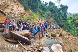 Người dân dùng xà beng, búa tạ phá nhỏ những tảng đá lớn tại điểm sạt lở trước khi kích nâng lên thanh trượt để dịch chuyển sang mép vực, tạo lối mở qua điểm sạt lở. (Ảnh: TTXVN phát)
