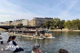 Tàu du lịch trên sông Seine đi qua những khu phố cổ của Paris, trong khi người dân ngồi nghỉ ngay sát mép nước. (Ảnh: Hữu Chiến/TTXVN)