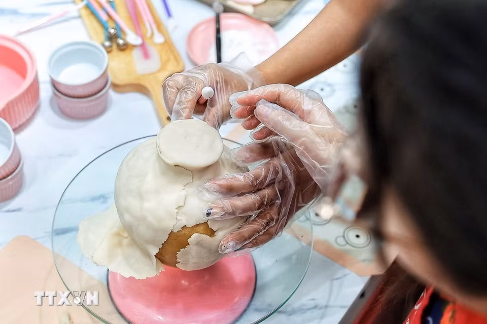 Người làm tỉ mỉ miết, chỉnh từng phần bột phủ bên ngoài của bánh Trung Thu để hoàn thiện hình dáng chiếc bình trước khi trang trí và kết hợp với những cành hoa tò he. (Ảnh: Phạm Tuấn Anh/TTXVN)
