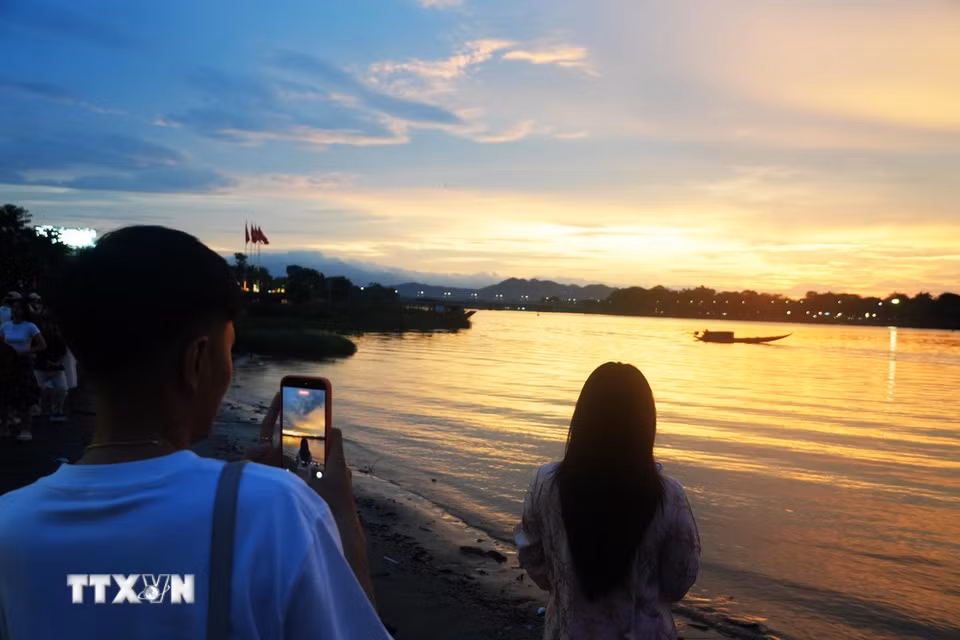 Giới trẻ chụp ảnh lưu lại cảnh đẹp của hoàng hôn từ bờ Nam sông Hương, thành phố Huế. (Ảnh: Nguyên Lý/TTXVN)