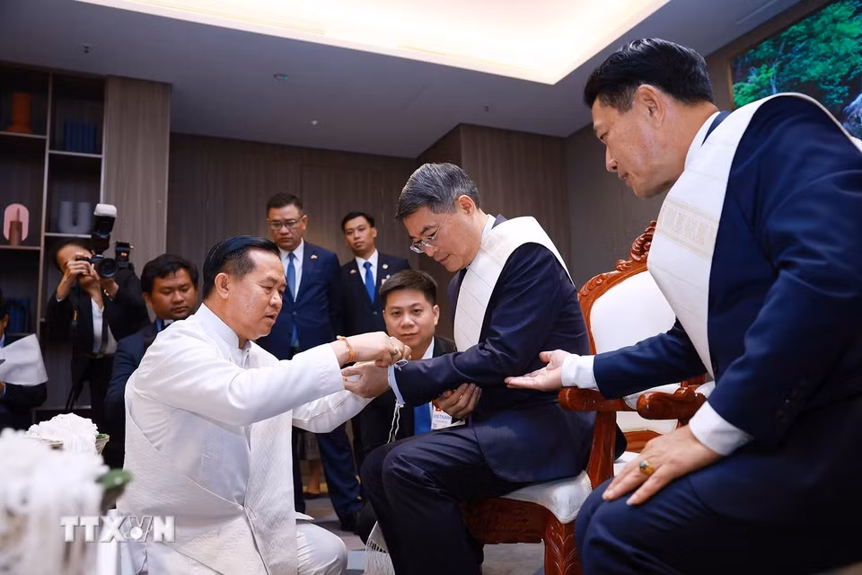 Thủ tướng Lê Minh Hưng thực hiện nghi thức buộc chỉ cổ tay truyền thống của Lào. (Ảnh: Dương Giang/TTXVN)