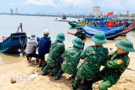 Cán bộ, chiến sỹ Đồn Biên phòng Nhật Lệ cùng người dân địa phương tổ chức cứu hộ thuyền cá bị chìm. (Ảnh: TTXVN phát)